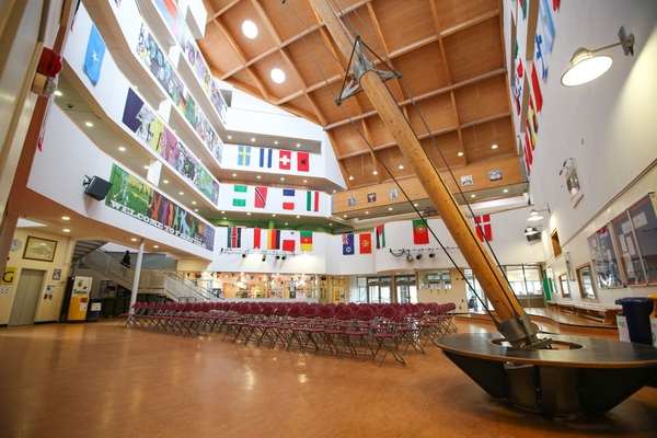 Love Locations modern school atrium shoot location Bristol BS7: Vast multi-story communal hall featuring a dramatic wood-panelled ceiling and rows of chairs, ideal for assembly scenes, TV dramas, and film productions.