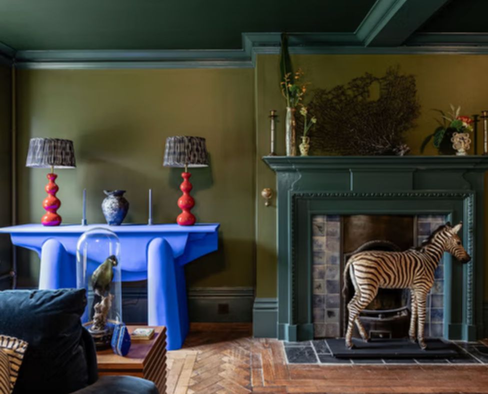 Olive-green living room at Fable with a jade fireplace, bright blue console table and colourful decorative styling.