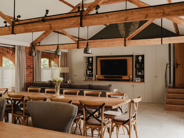 Open-plan living space in a converted Oxfordshire barn showing a large dining table, plush seating, and exposed timber framing, Love Locations.
