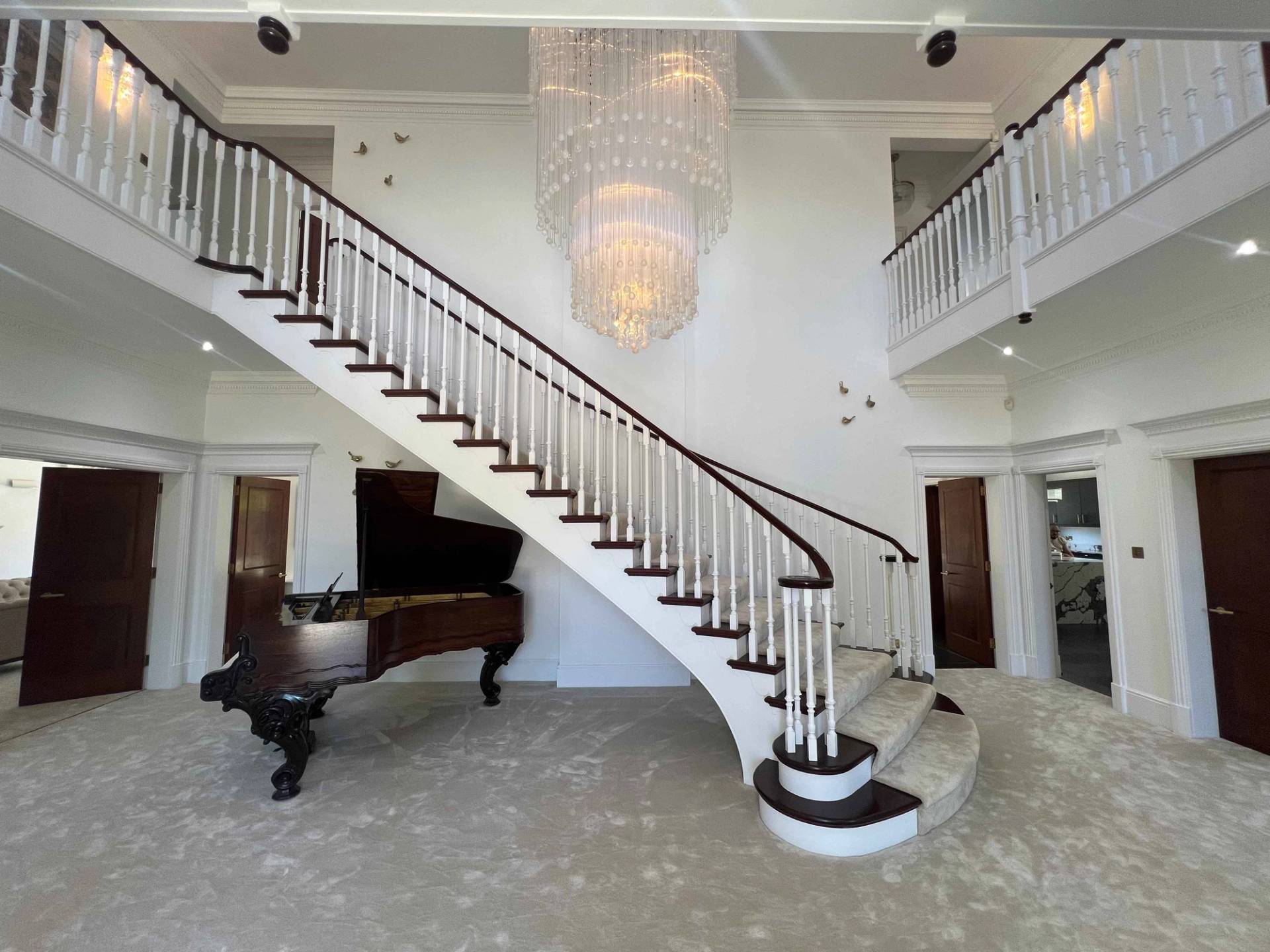 Double-height entrance foyer featuring a sweeping curved staircase, grand piano, crystal chandelier, and galleried landing, Love Locations BR7.
