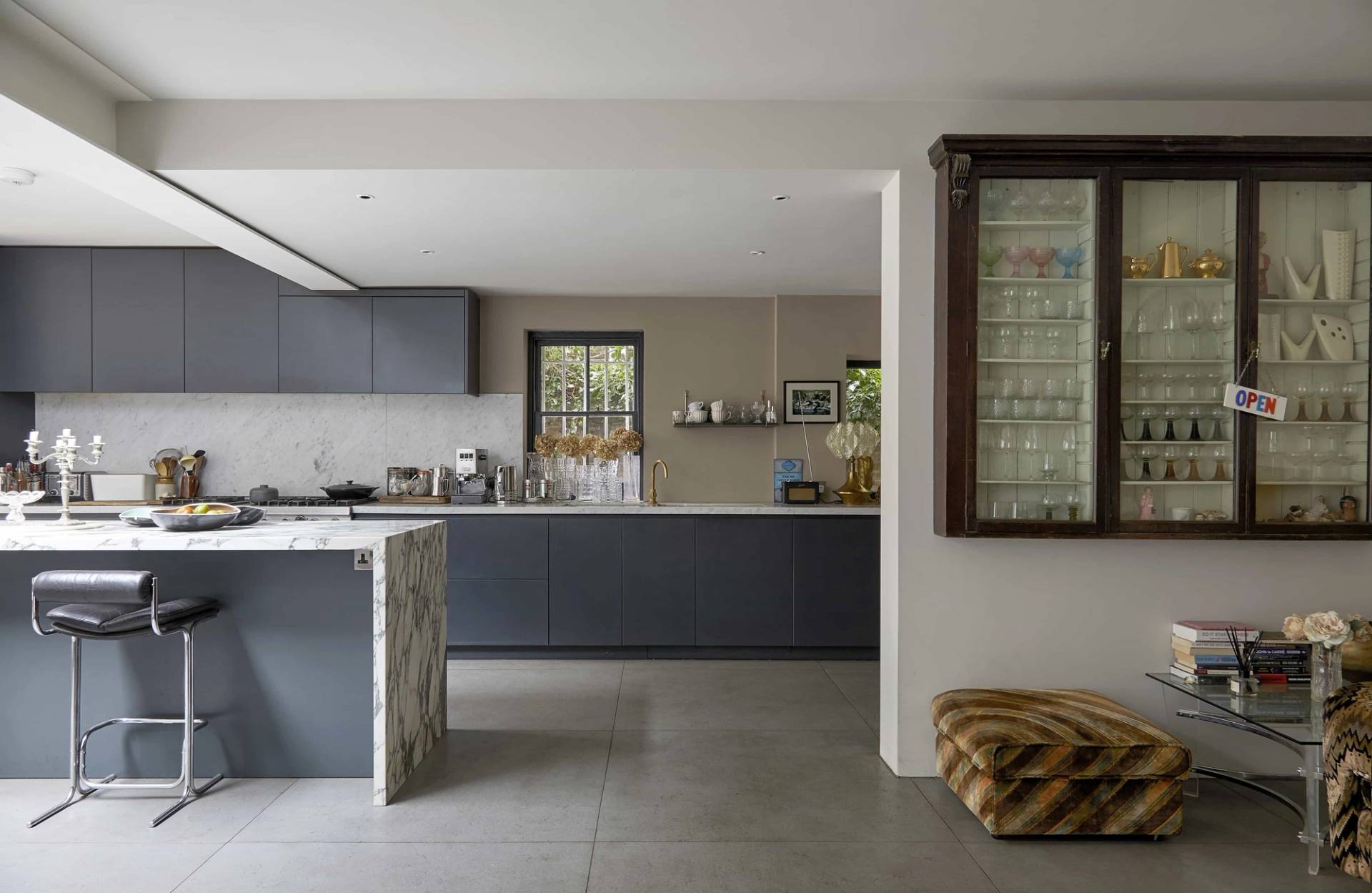 Kitchen extension transition looking from dark grey cabinetry past a marble island into a garden dining nook, Love Locations N16.