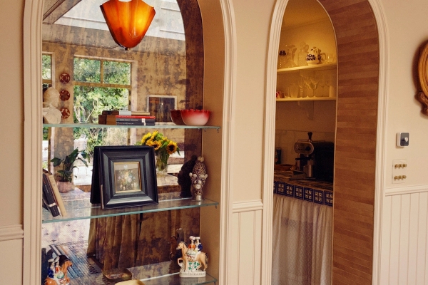 Glass display shelving unit filled with vintage ceramics and ornaments set inside a warm architectural archway, Love Locations.
