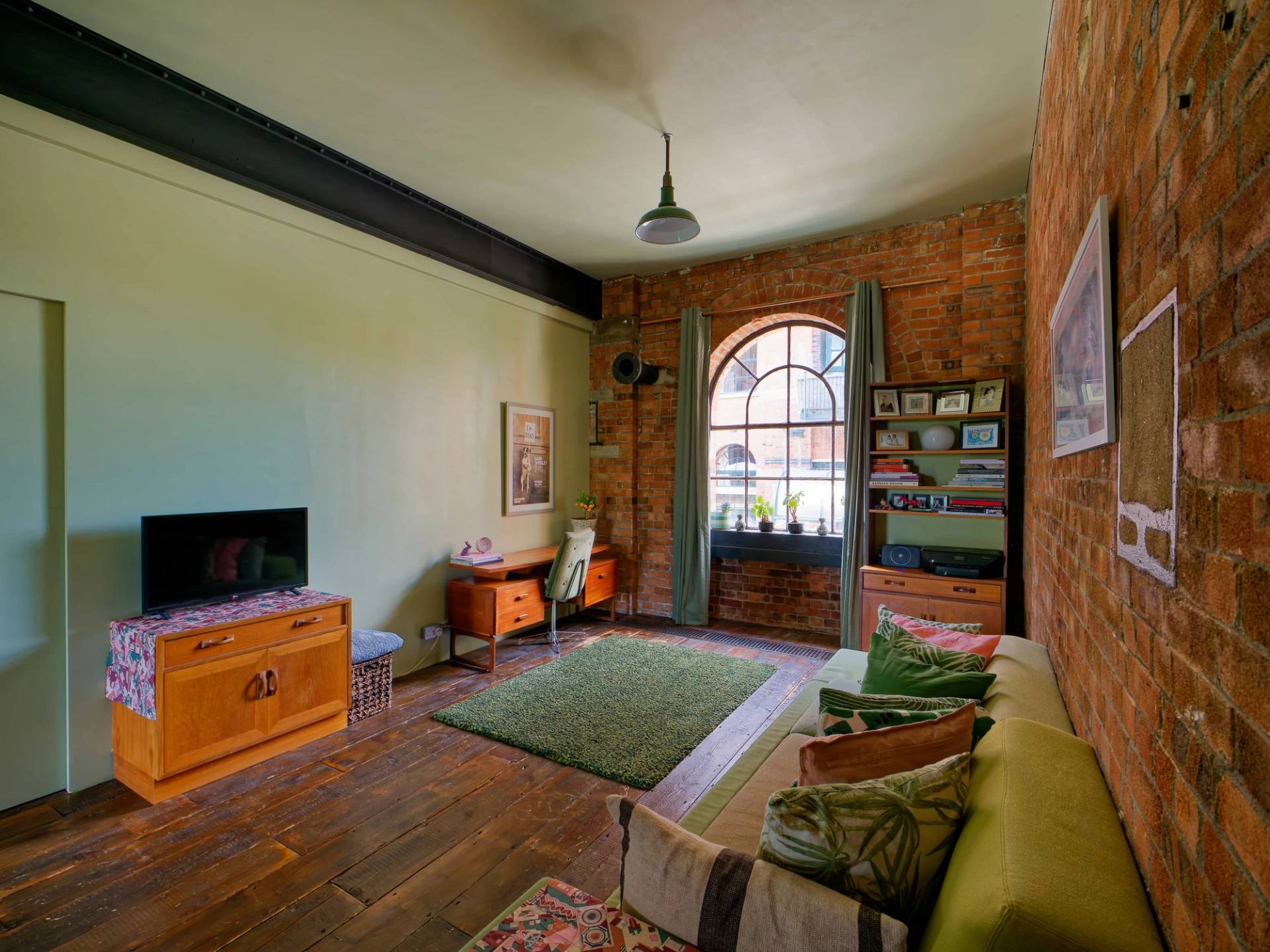 Loft sitting room featuring exposed red brick walls, arched window, green sofa, and timber flooring, ideal for brand shoots, Love Locations.