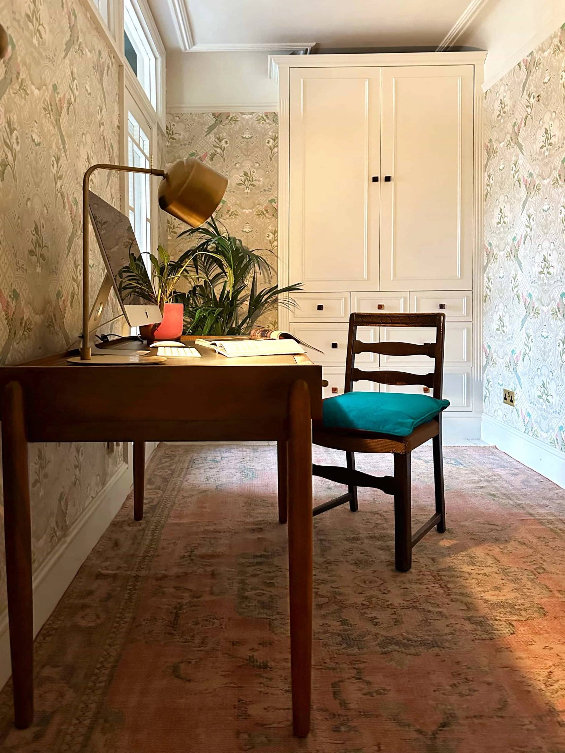 Home workspace with wooden writing desk, teal armchair, built-in storage, and brick flooring, Love Locations N13.