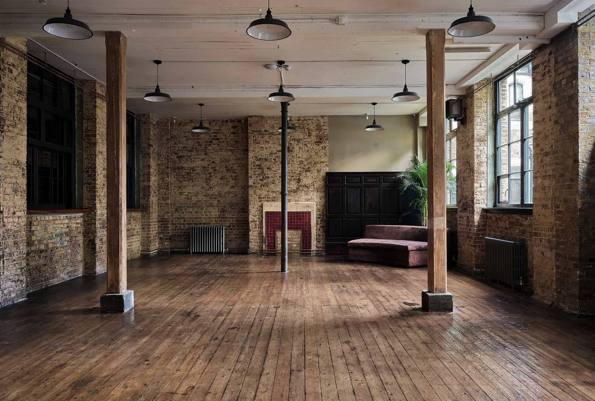 Industrial warehouse hall venue featuring exposed brick walls, timber support pillars, and polished dark wood floors, ideal for music video shoots, Love Locations.