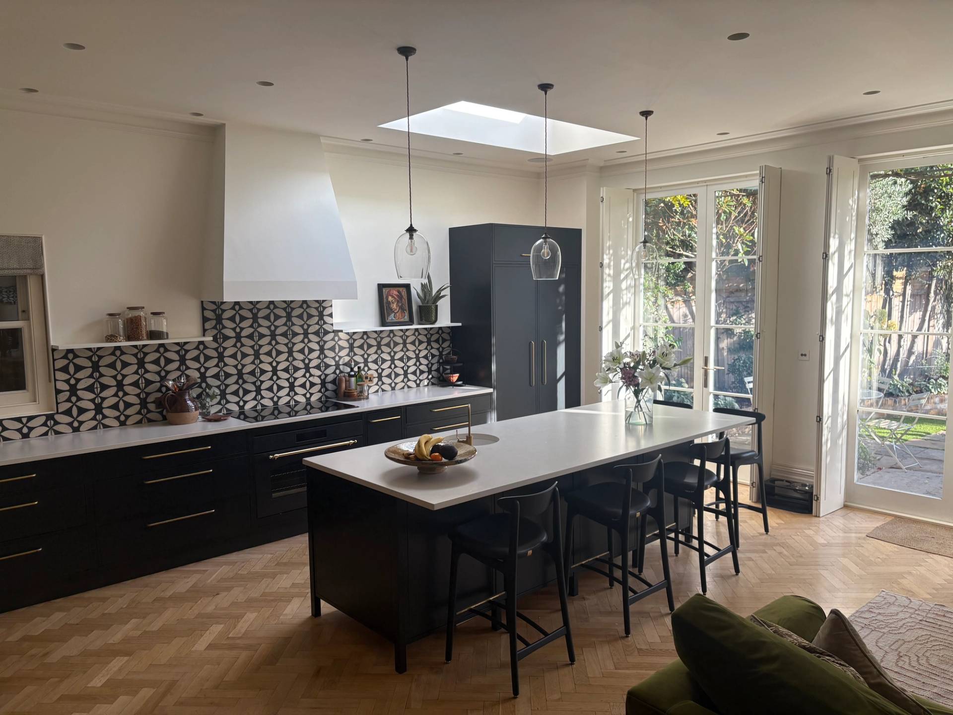  Modern kitchen shoot space in a Victorian home in Twickenham TW1 from Love Locations, featuring a central kitchen island with bar stools, dark cabinetry, white marble countertops, and skylights.