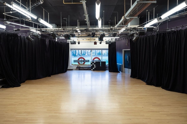 Love Locations black box drama studio Bristol: Performing arts space featuring full-length black blackout curtains, overhead lighting tracks, and a wooden floor, tailored for independent film sets and interviews.