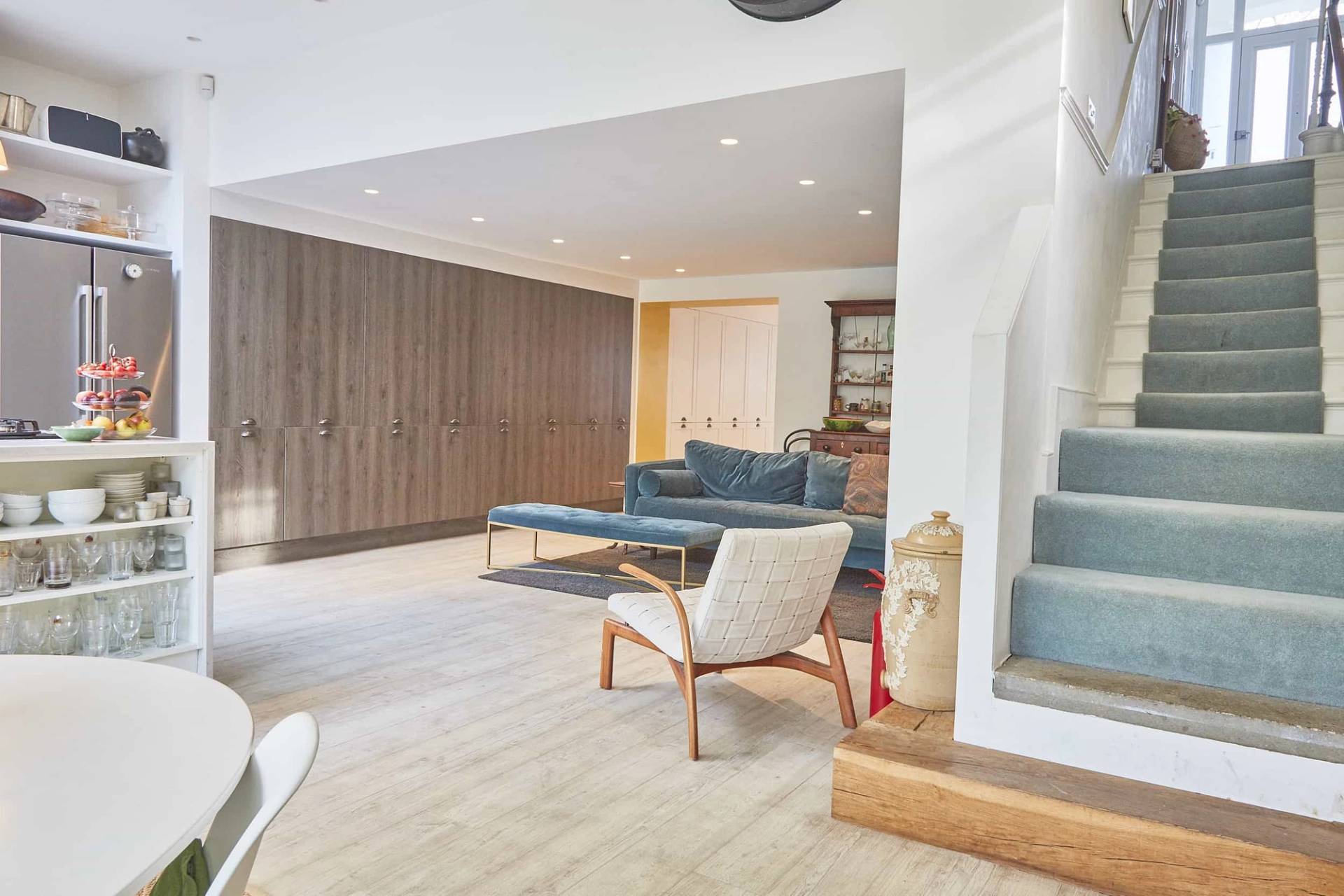 Open-plan living room transition with mid-century armchair, wood-panelled storage wall, and light timber floorboards, Love Locations.