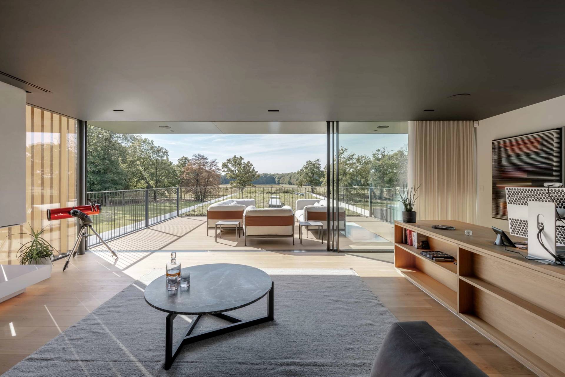 Contemporary indoor-outdoor lounge area featuring a round coffee table and floor-to-ceiling sliding glass doors opening to rural Essex views, Love Locations.