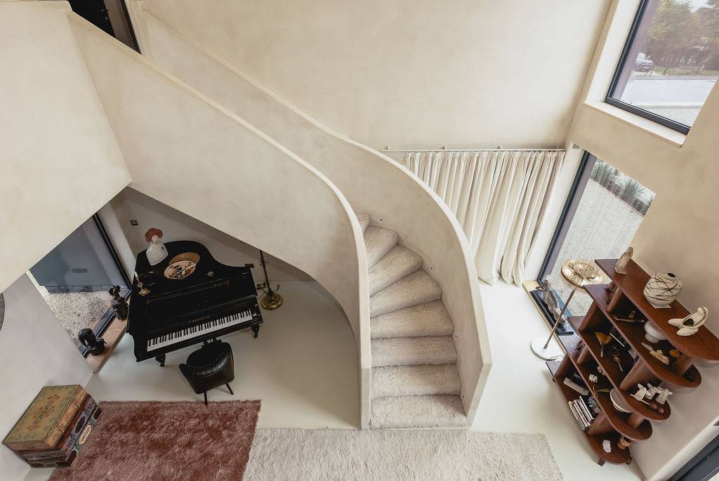 High-angle perspective looking down a curved microcement plaster staircase toward a grand piano, Love Locations GU32.
