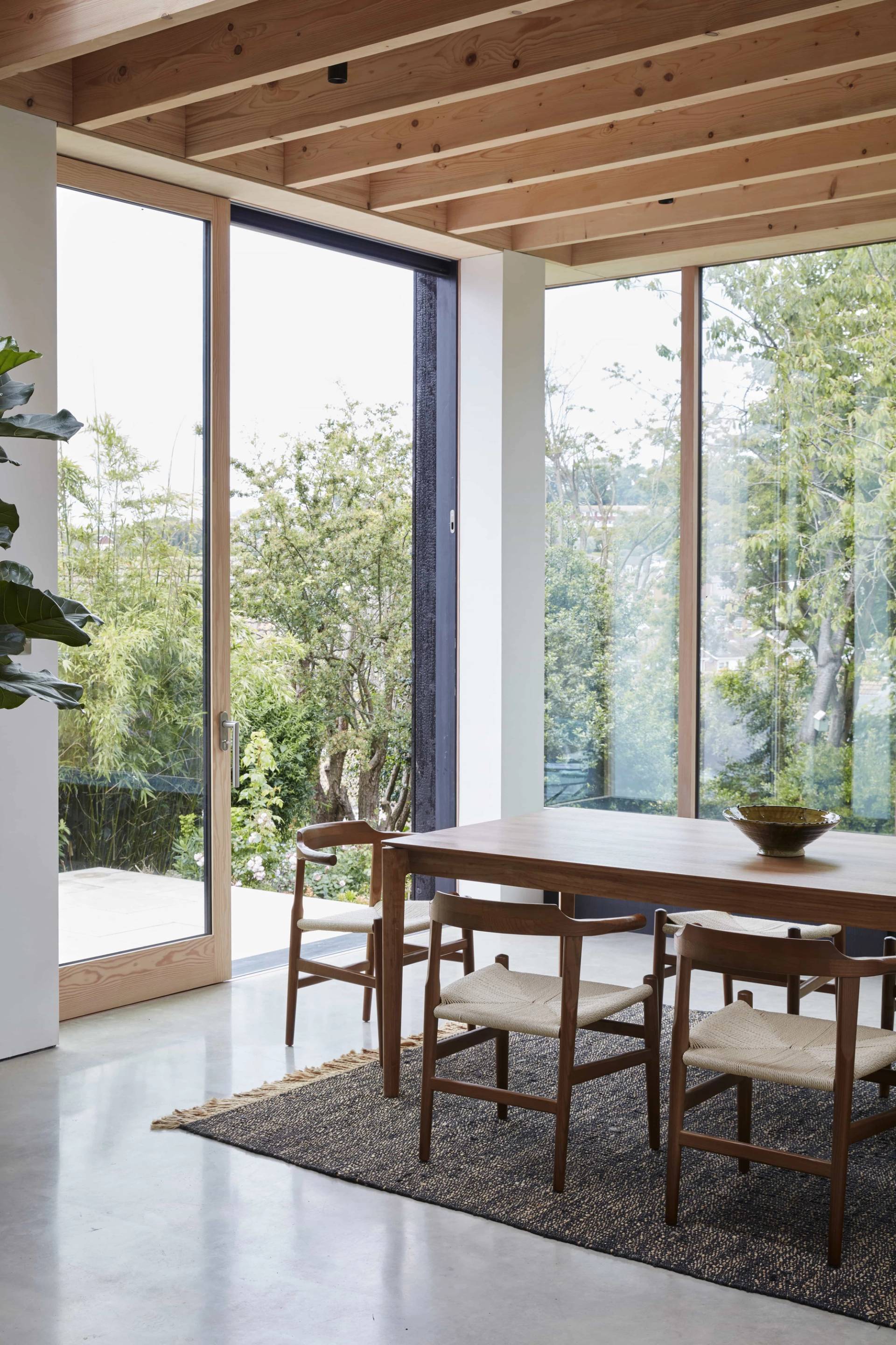 Light oak dining table set inside an open-plan glass timber extension overlooking garden foliage, perfect for food editorial media, Love Locations.