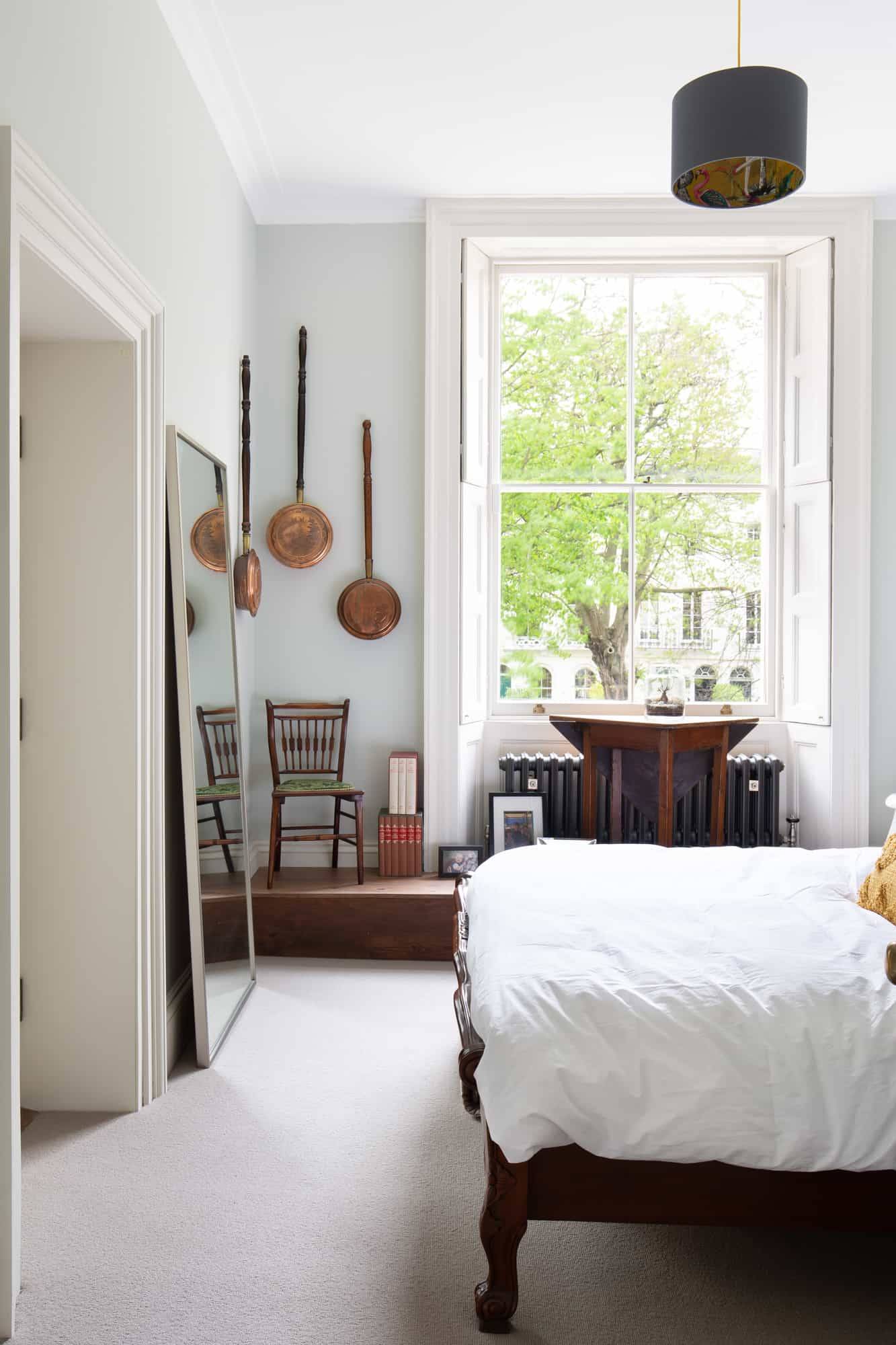Sunlit white bedroom in SE5 with copper bed headboard, sash window shutters, and period details via Love Locations.