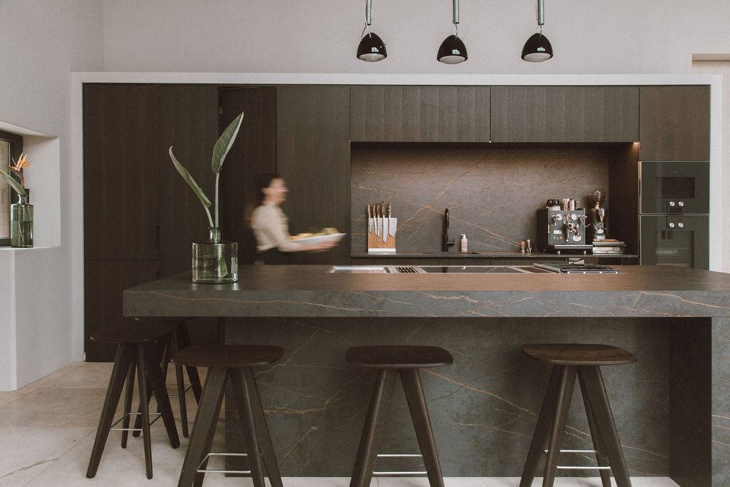 Modern luxury villa location in Mallorca, 07630 featuring a dark textured kitchen island counter, bar stools, and black pendant lights via Love Locations.