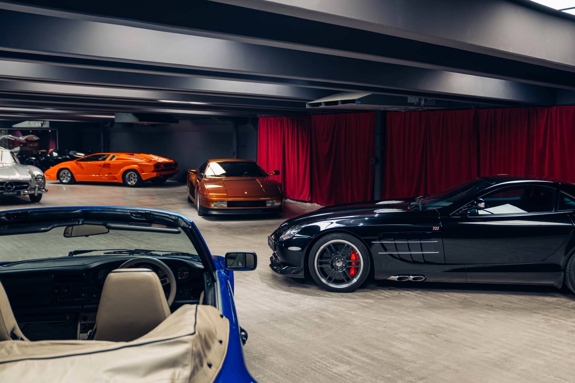 Moody underground lounge and supercar vault featuring dark leather seats, red velvet drapes, and hypercars through Love Locations.