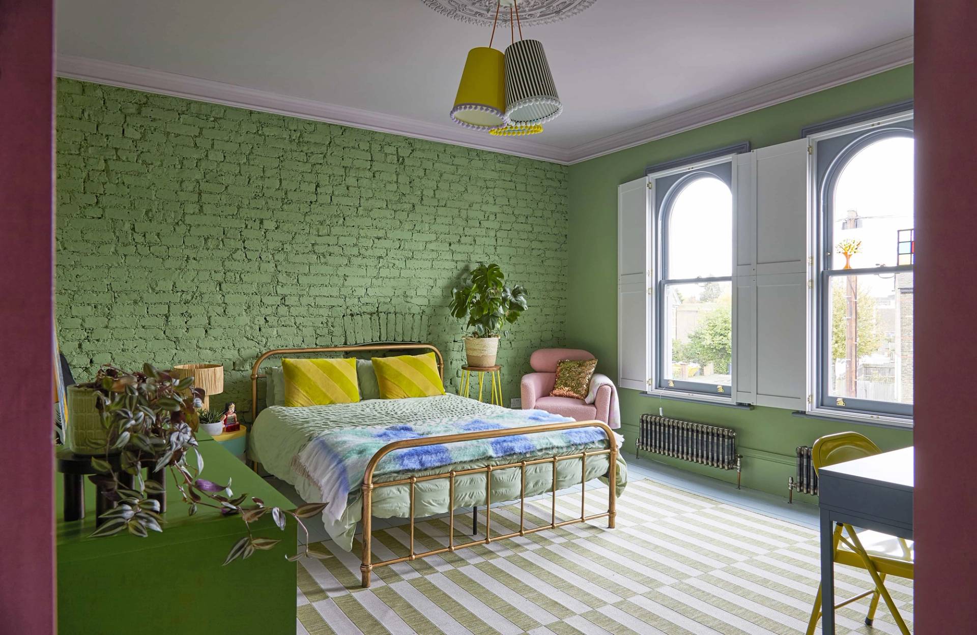 Pistachio green bedroom with exposed green brick accent wall, brass bed frame, and striped rug, Love Locations Catford.