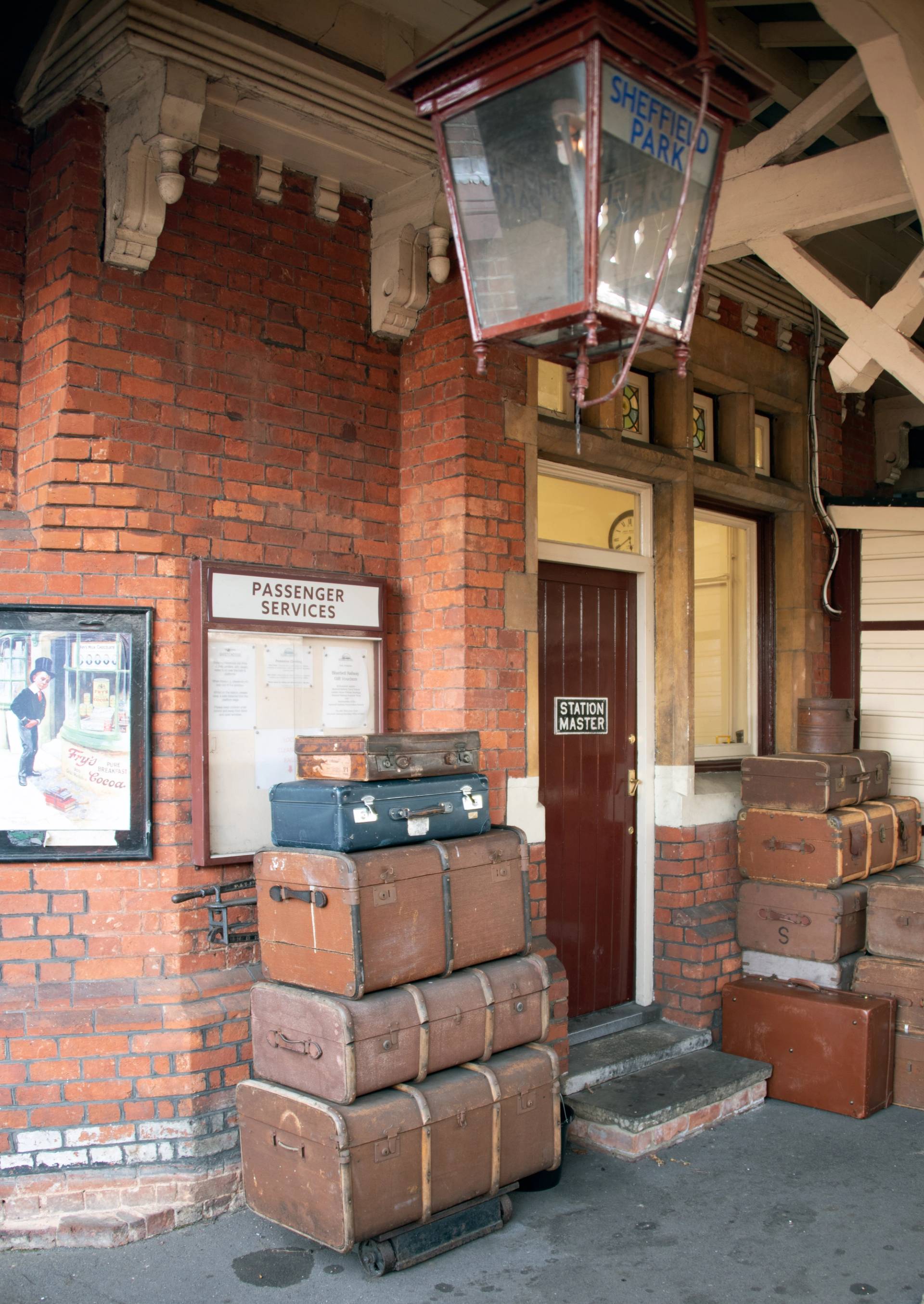 Red brick station building exterior with stacked vintage leather luggage and ticket office doors in Sussex, Love Locations TN22 3QL.