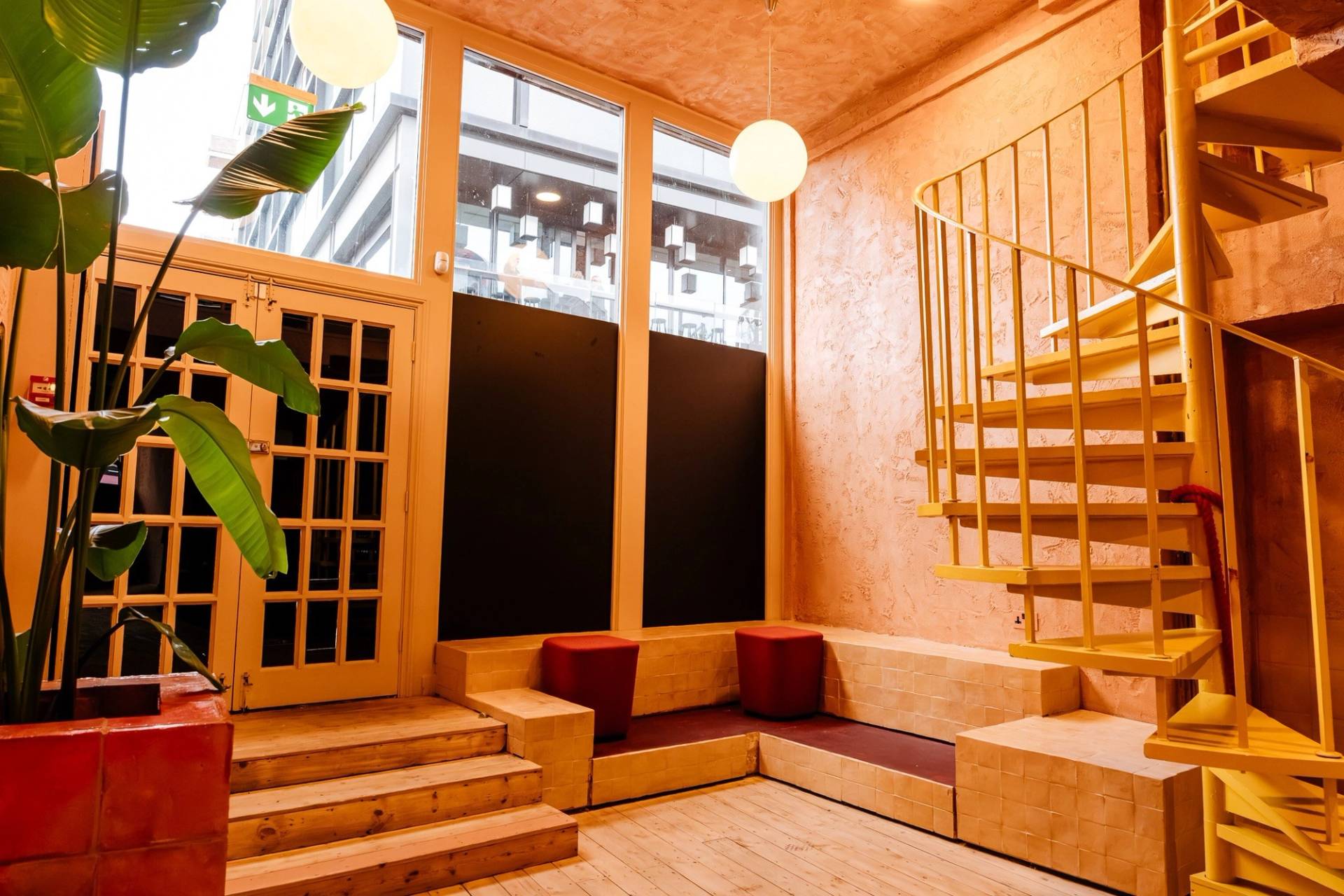 Terracotta-toned bar lounge nook with a yellow spiral staircase, glass double doors, and integrated bench seating via Love Locations.