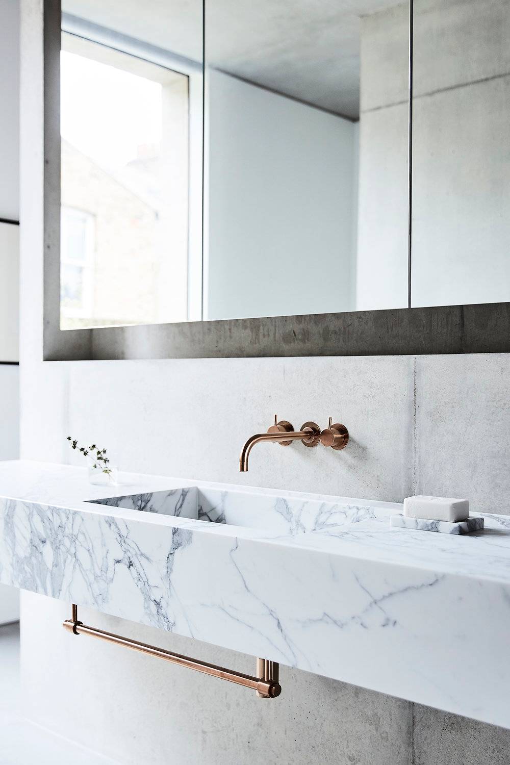Luxury modern bathroom vanity setup showcasing a custom white marble sink basin, copper wall-mounted taps, and frameless mirror, ideal for grooming brand campaigns, Love Locations SW8.