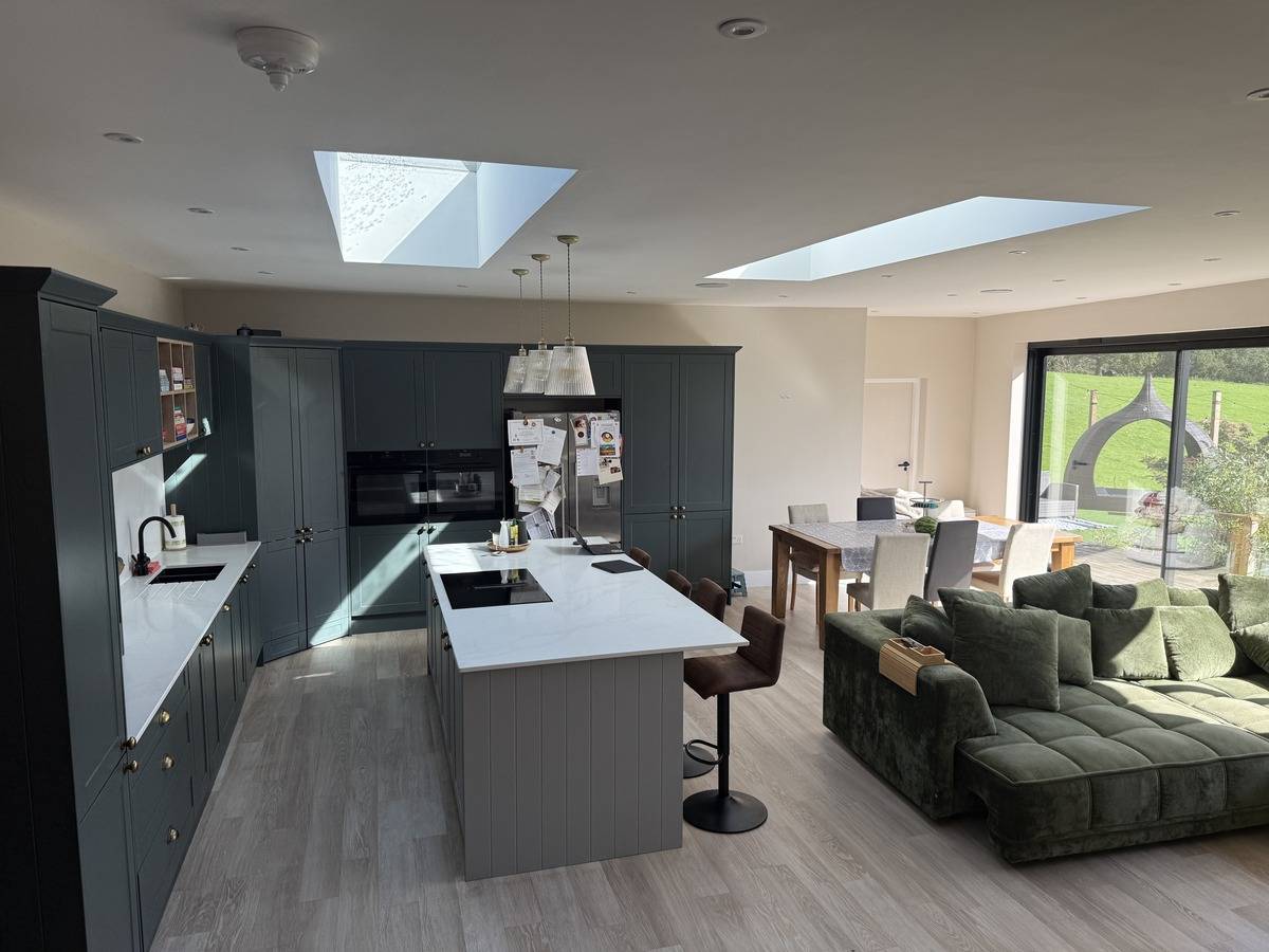 Bright open-plan kitchen and dining area in a detached family location house in Stockport SK6 from Love Locations, featuring a grey kitchen island, roof skylights, and double bi-fold doors.