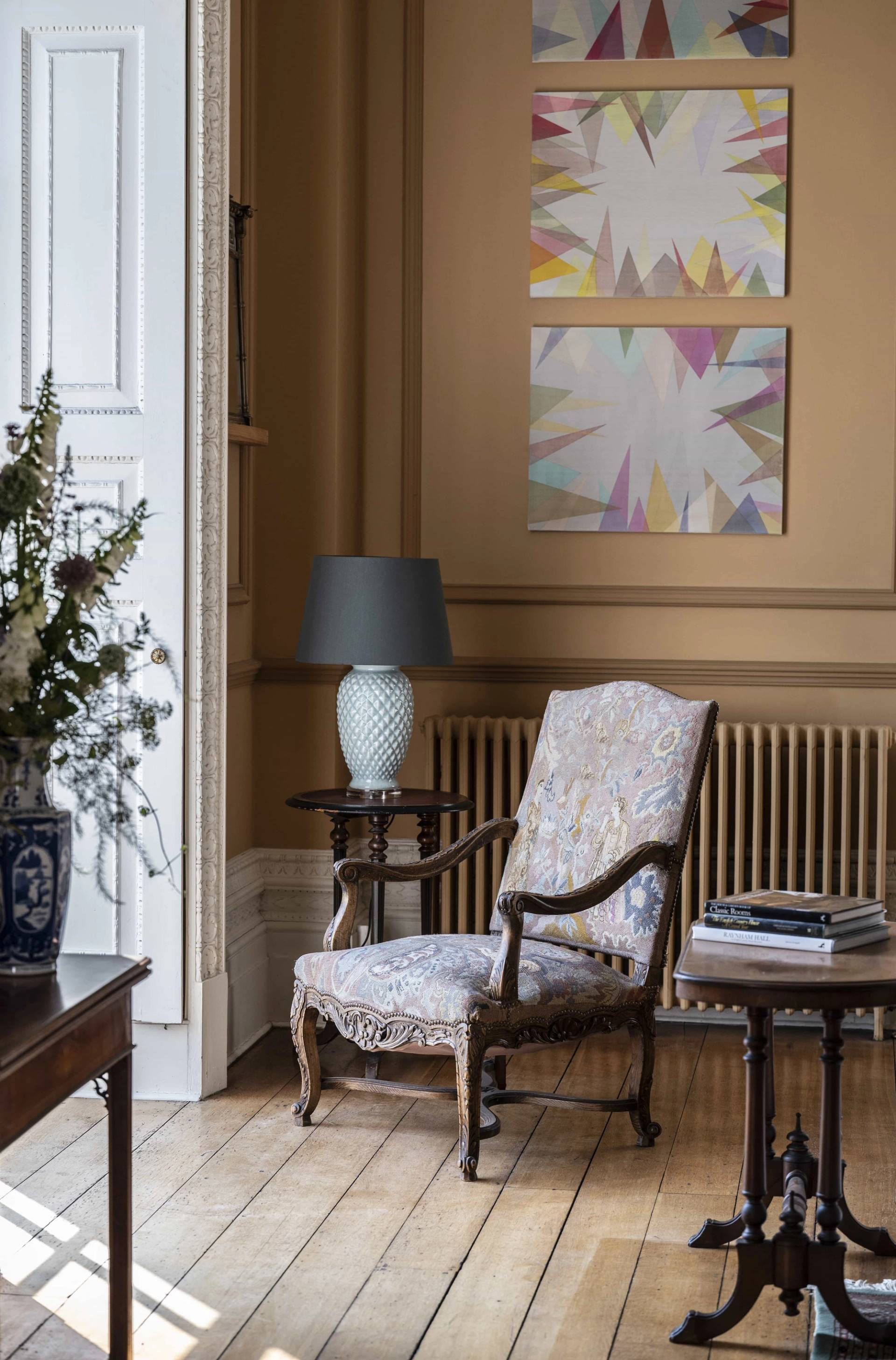 Classic floral armchair set beside a small side table and sash window in an ochre reception room, Love Locations LE7.