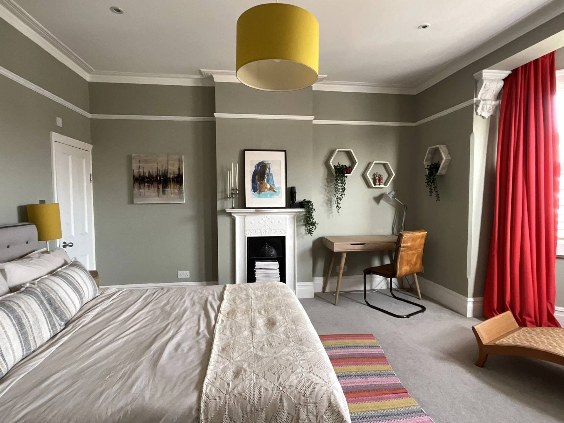 Olive green bedroom featuring a white period fireplace hearth, small wooden desk nook, and geometric wall shelves, Love Locations W3.