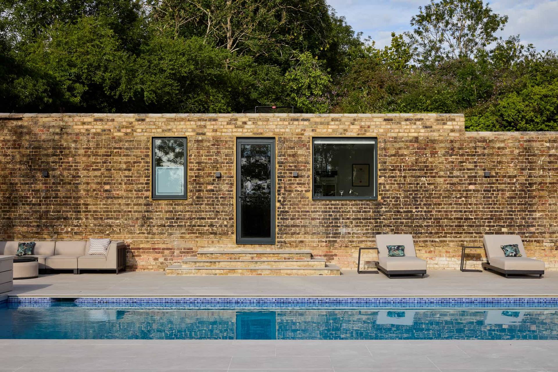 Outdoor swimming pool with sun loungers set beside a traditional yellow brick wall in a Surrey luxury location house, ideal for summer lifestyle campaigns, Love Locations KT22.