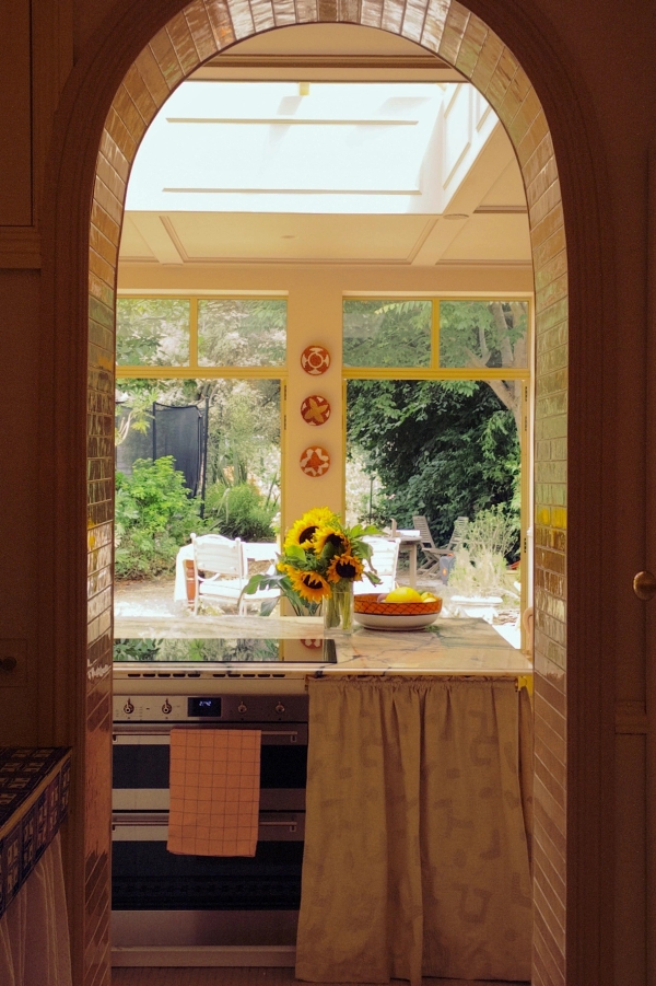 Archway view from a rustic kitchen looking out through large windows onto a lush green garden filled with sunflowers, perfect for idyllic summer drama filming, Love Locations.