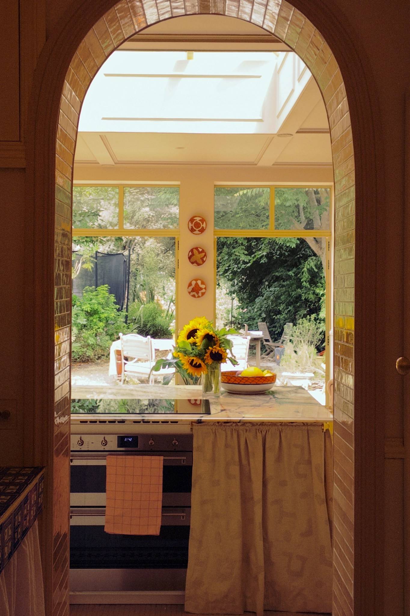 Archway view from a rustic kitchen looking out through large windows onto a lush green garden filled with sunflowers, perfect for idyllic summer drama filming, Love Locations.