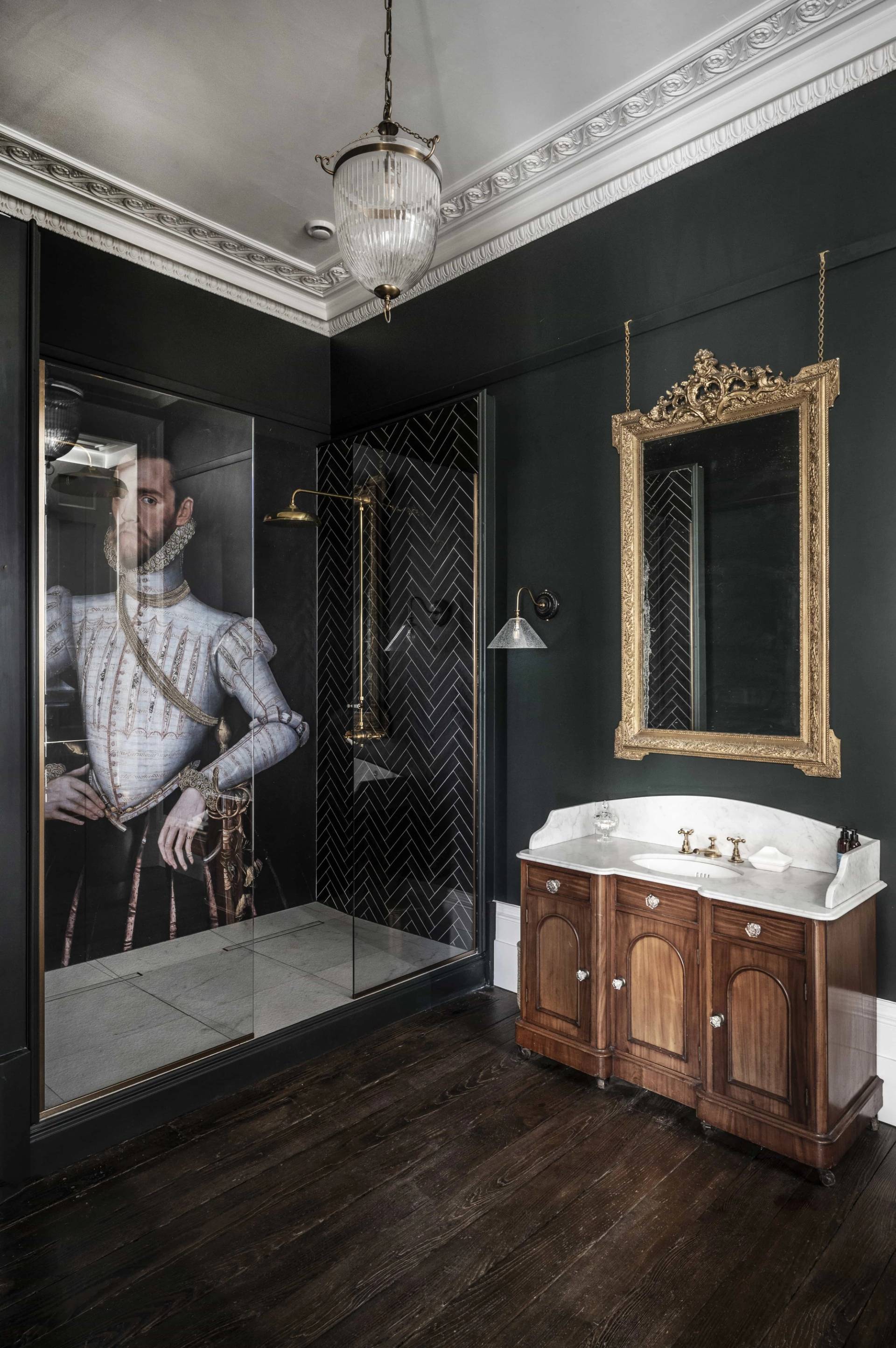 Bespoke bathroom vanity with a carved wooden cabinet, dark marble counter, and Elizabethan portrait shower backdrop, Love Locations LE7.