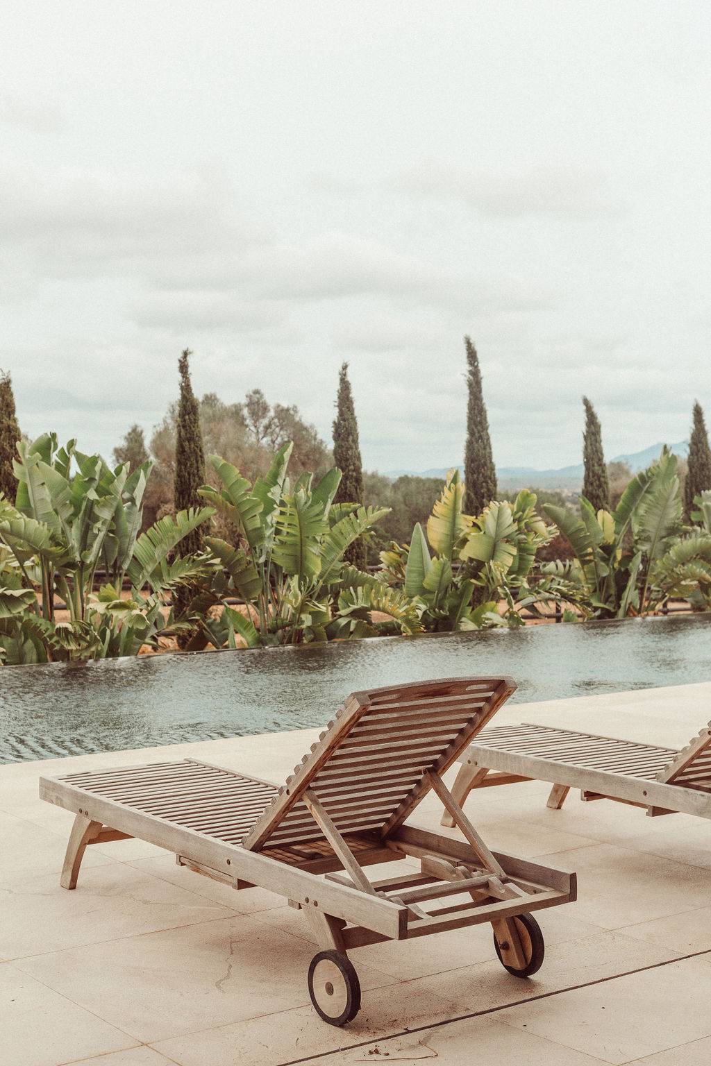 Outdoor infinity pool set amidst tropical palm trees, cypress hedges, and stone estate walls, Love Locations 07630.