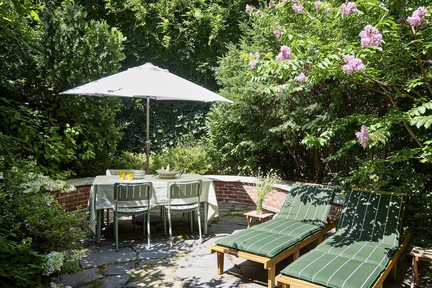 Secluded outdoor garden patio location for film and photography in Manhattan NYC via Love Locations, featuring a patio dining table, patio umbrella, sun lounger, and surrounding green garden brick walls.