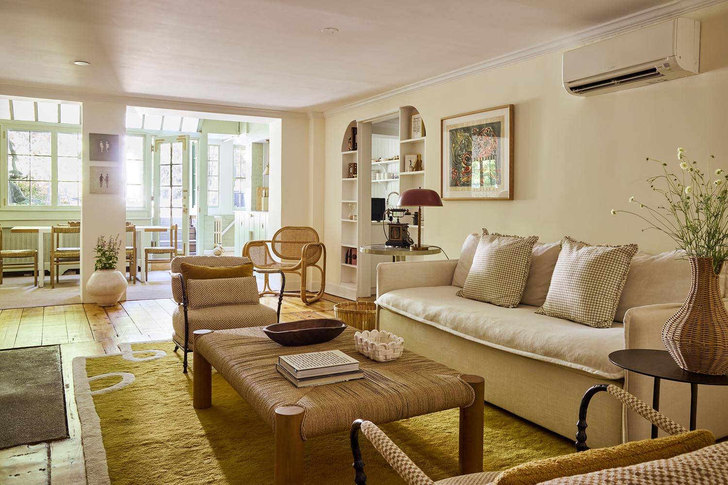 Sunlit garden-level living room film location in Manhattan New York NY 10014 from Love Locations, featuring cream plush sofas, a woven rope coffee table, neutral rug, and glass conservatory door transition.
