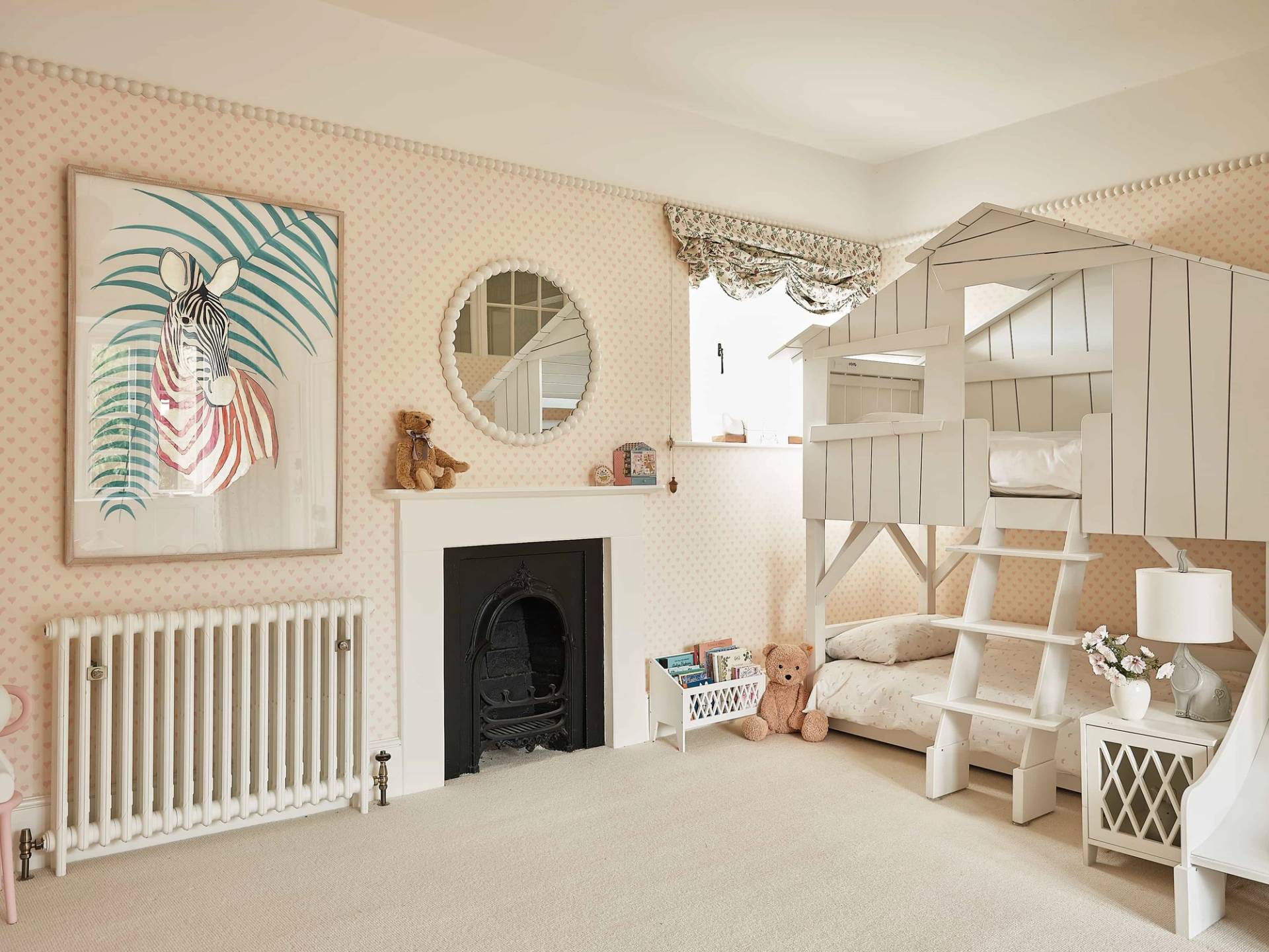 Charming children's bedroom featuring a cast iron fireplace hearth, circular mirror, and built-in treehouse bunk bed, ideal for family brand campaigns, Love Locations.