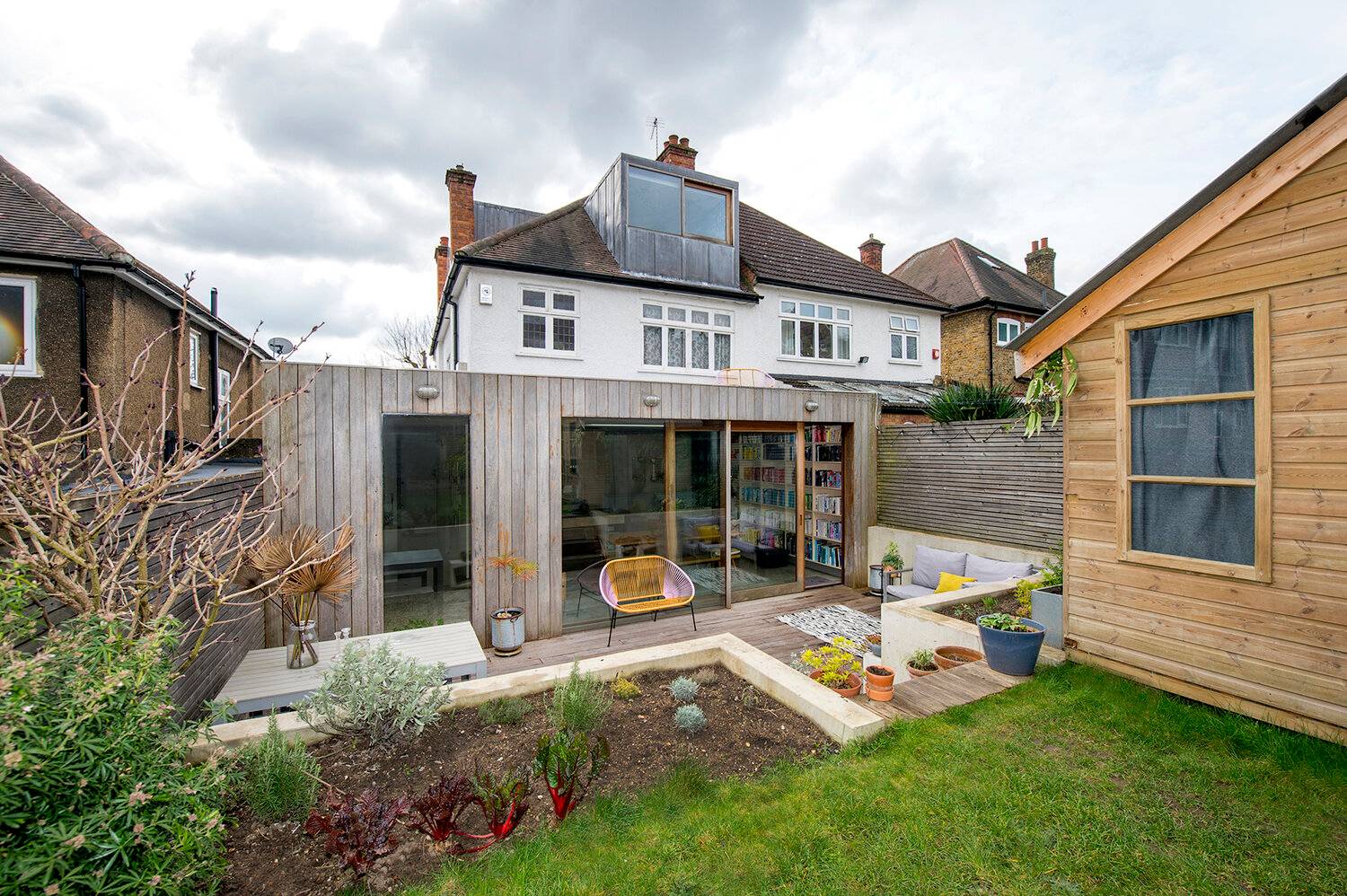 Architectural rear elevation of a timber-clad extension showing full-height glass sliding doors and tiered garden decking, Love Locations SE23.