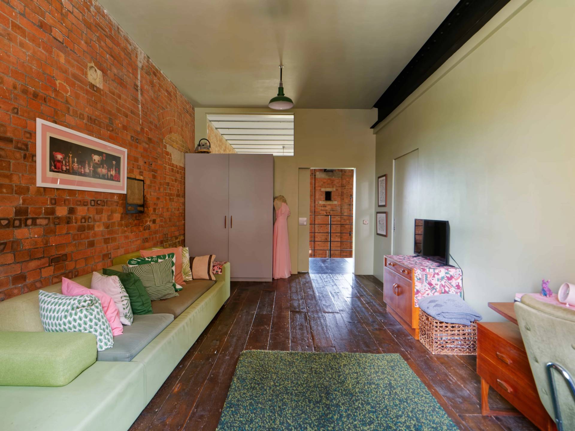 Spacious brick-walled room with long green built-in sofa bench, sage green rug, and vintage wooden chest, Love Locations E14.