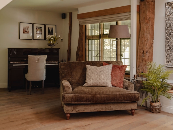Cozy velvet armchair reading corner positioned beside traditional leaded grid windows and oak pillars, Love Locations.