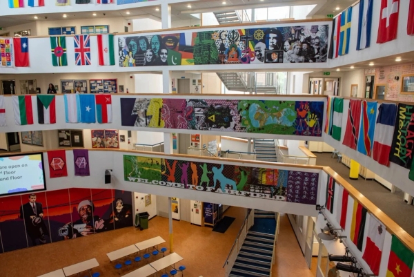 Love Locations contemporary school location Bristol: High-angle view across open balconies, staircases, and vibrant mural artwork in a communal main hall, tailored for TV series tracking shots.