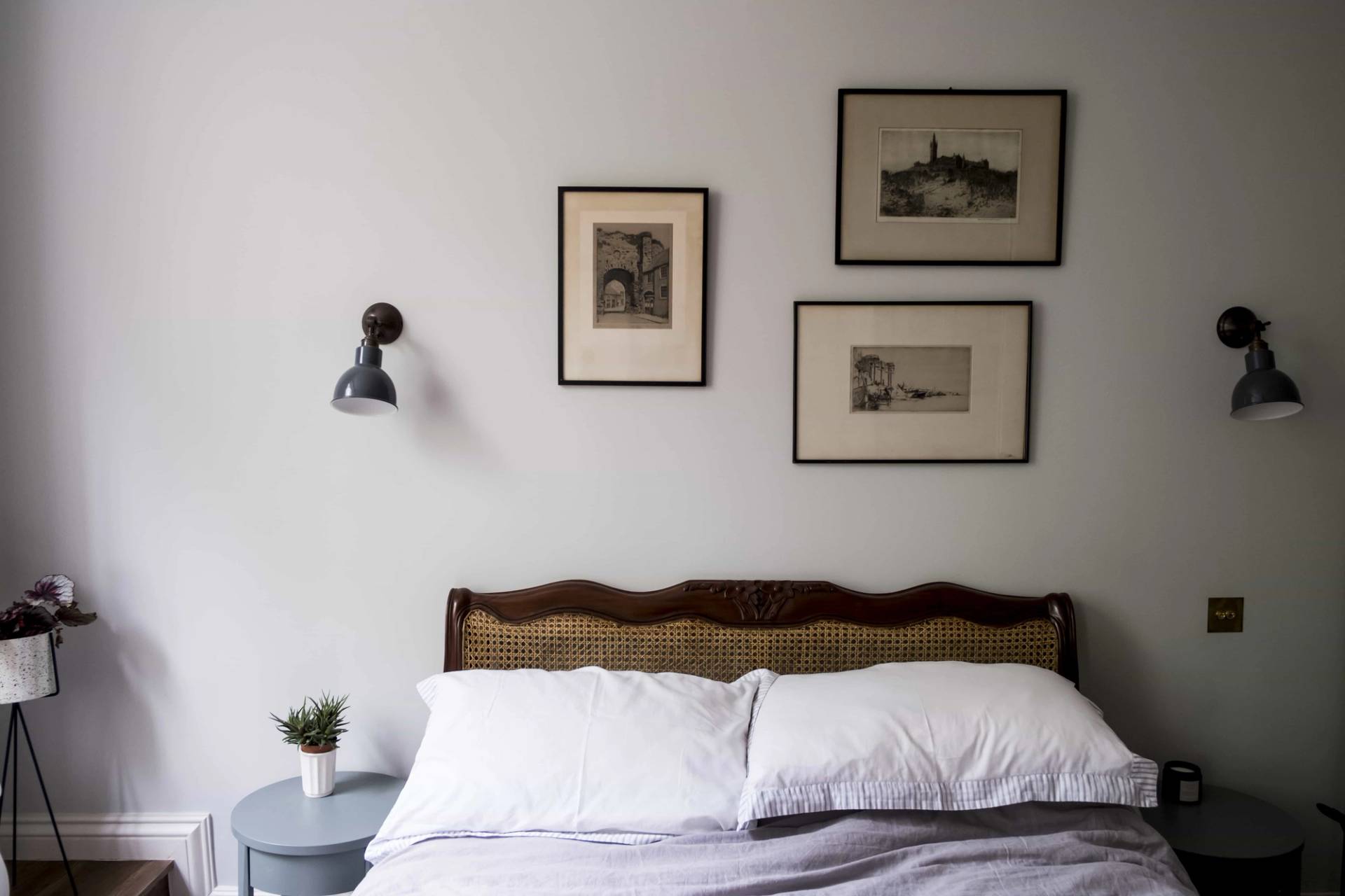 Bedroom corner setup with rattan bed frame, wall-mounted reading lights, and simple artwork in SE5 via Love Locations.