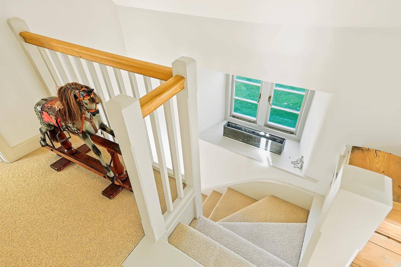 Characterful wooden cottage staircase shoot location in Gloucestershire GL7 via Love Locations, featuring a wooden banister, carpeted winding stairs, and a vintage rocking horse.