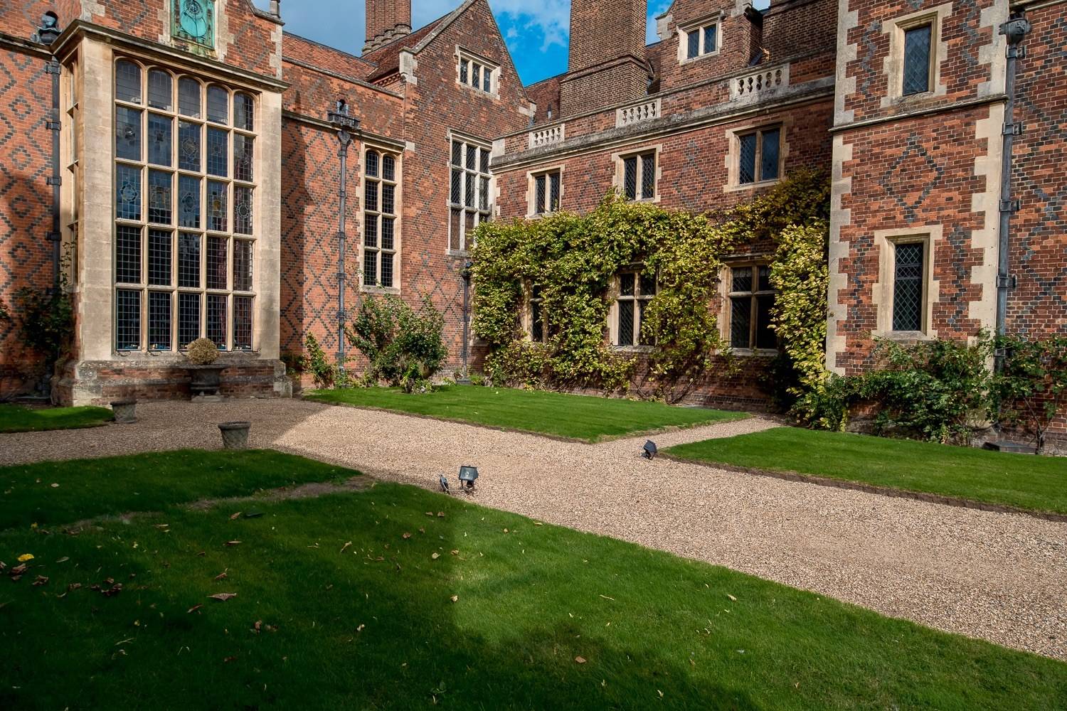 Red-brick Elizabethan manor house inner courtyard with ivy-covered walls and gravel path from Love Locations.