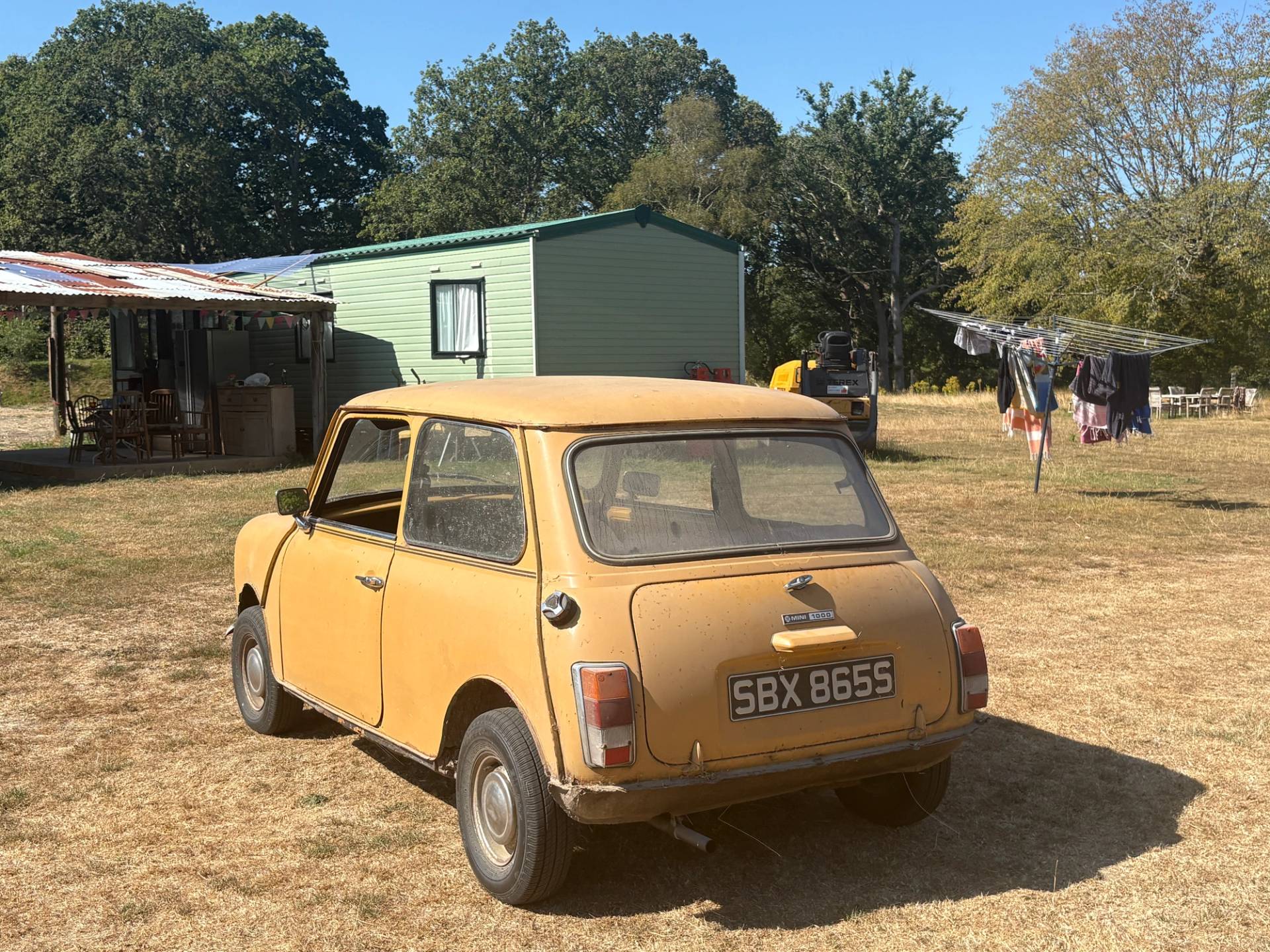 Vintage yellow Classic Mini car parked on an industrial farm field beside corrugated farm buildings in South Chailey, Love Locations BN8.