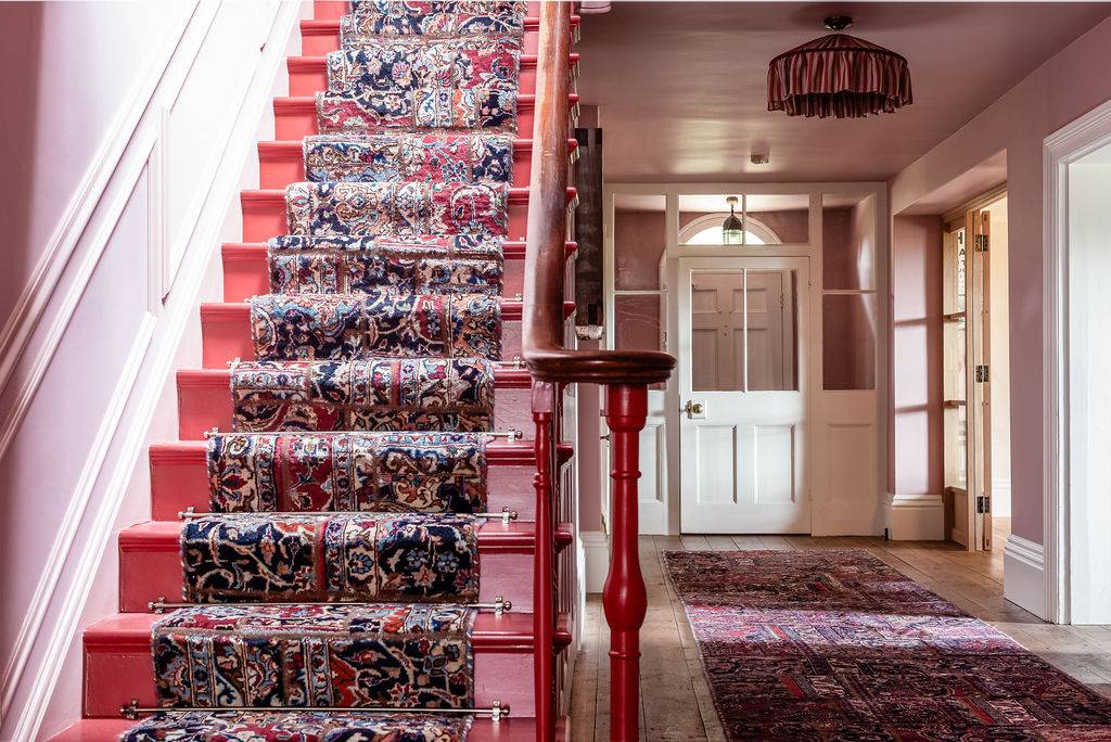 Looking up a stately staircase with a vintage patterned runner rug, showcasing a luxury country house entrance available through Love Locations.
