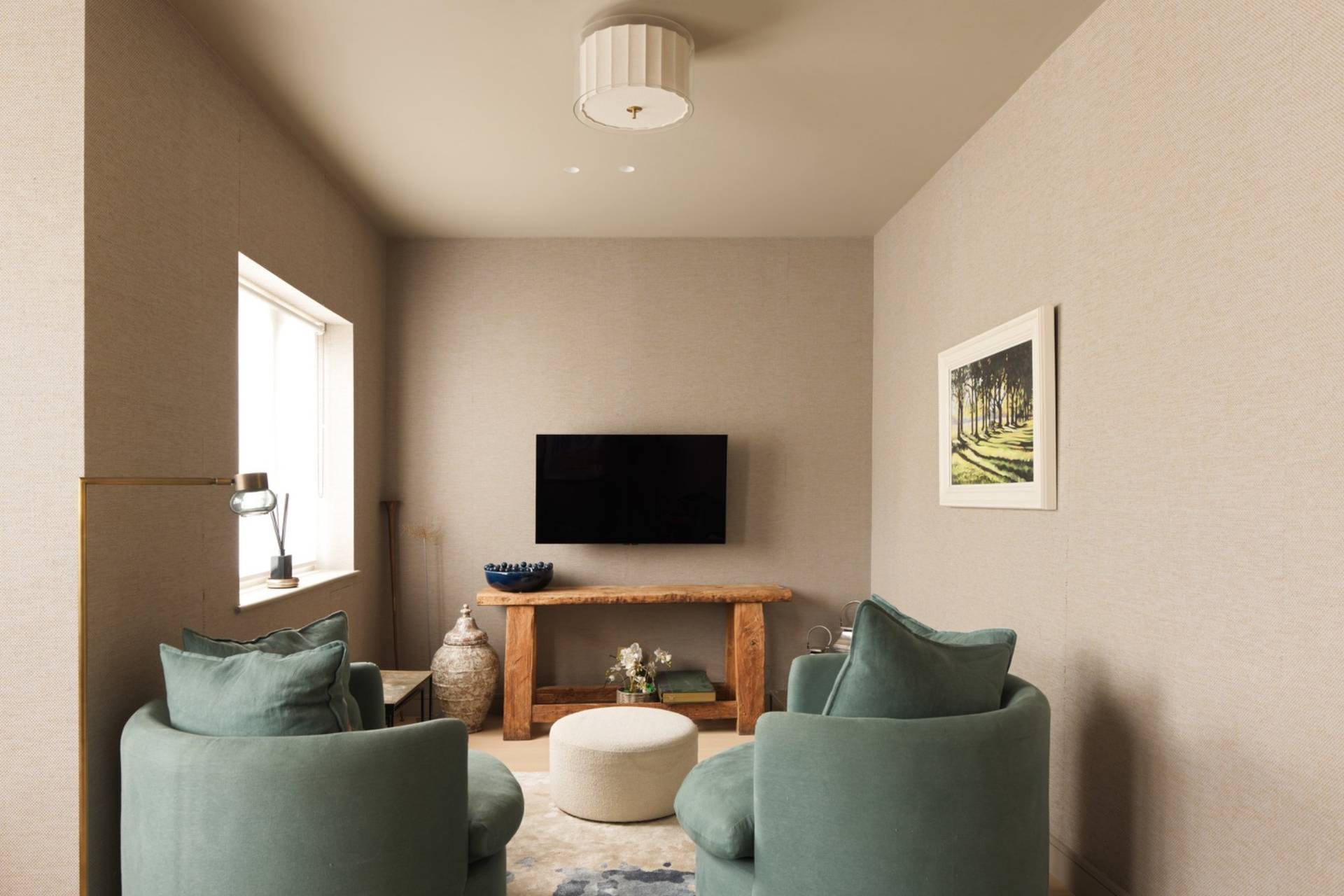 Cozy snug TV room with sage green armchairs, wooden media unit, and neutral walls through Love Locations.