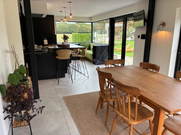 Open-plan dining and kitchen shoot location in Essex CM4 from Love Locations, showcasing a large natural wood dining table with matching wooden chairs and garden views.