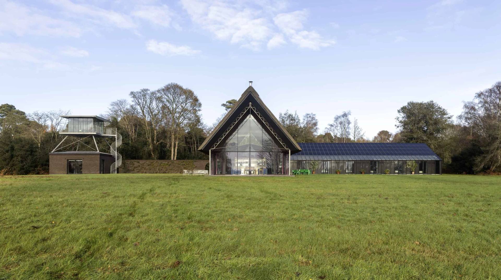 Front view of a modern thatched longhouse with full glass gabled elevation set across open lawns, Love Locations IP17.