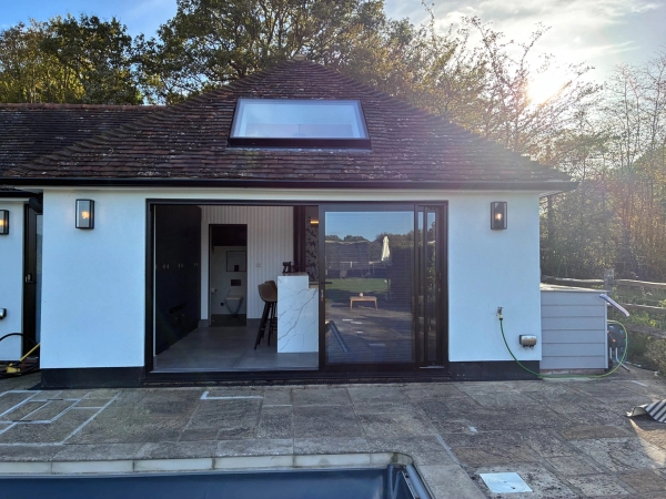 Modern outbuilding or pool house shoot location in Essex CM4 by Love Locations, featuring large black-framed glass sliding doors opening onto the pool deck.