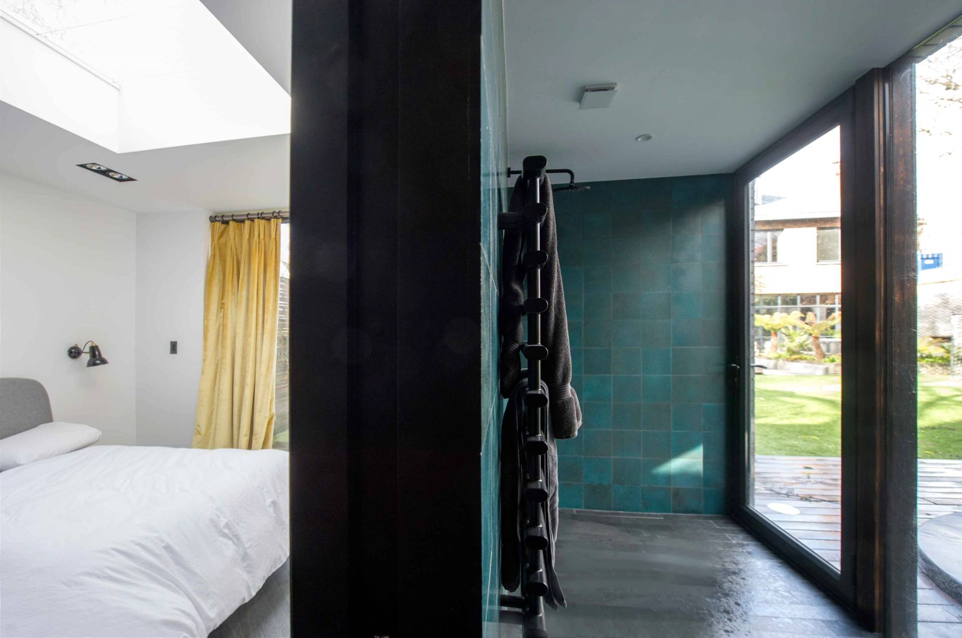 Sleek minimalist bedroom corner featuring floor-to-ceiling windows, soft natural light, and a stylish tiled ensuite wet room partition, Love Locations NW3.