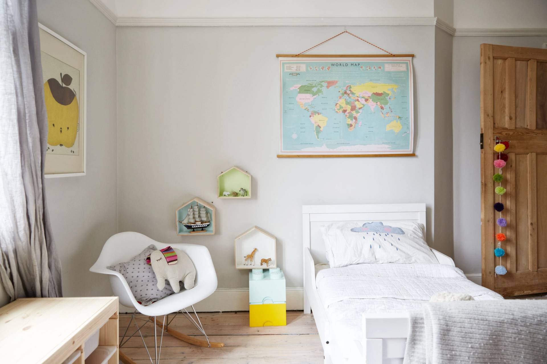 Children's nursery bedroom with white wooden bed, world map wall hangings, and small rocking chair, Love Locations N13.