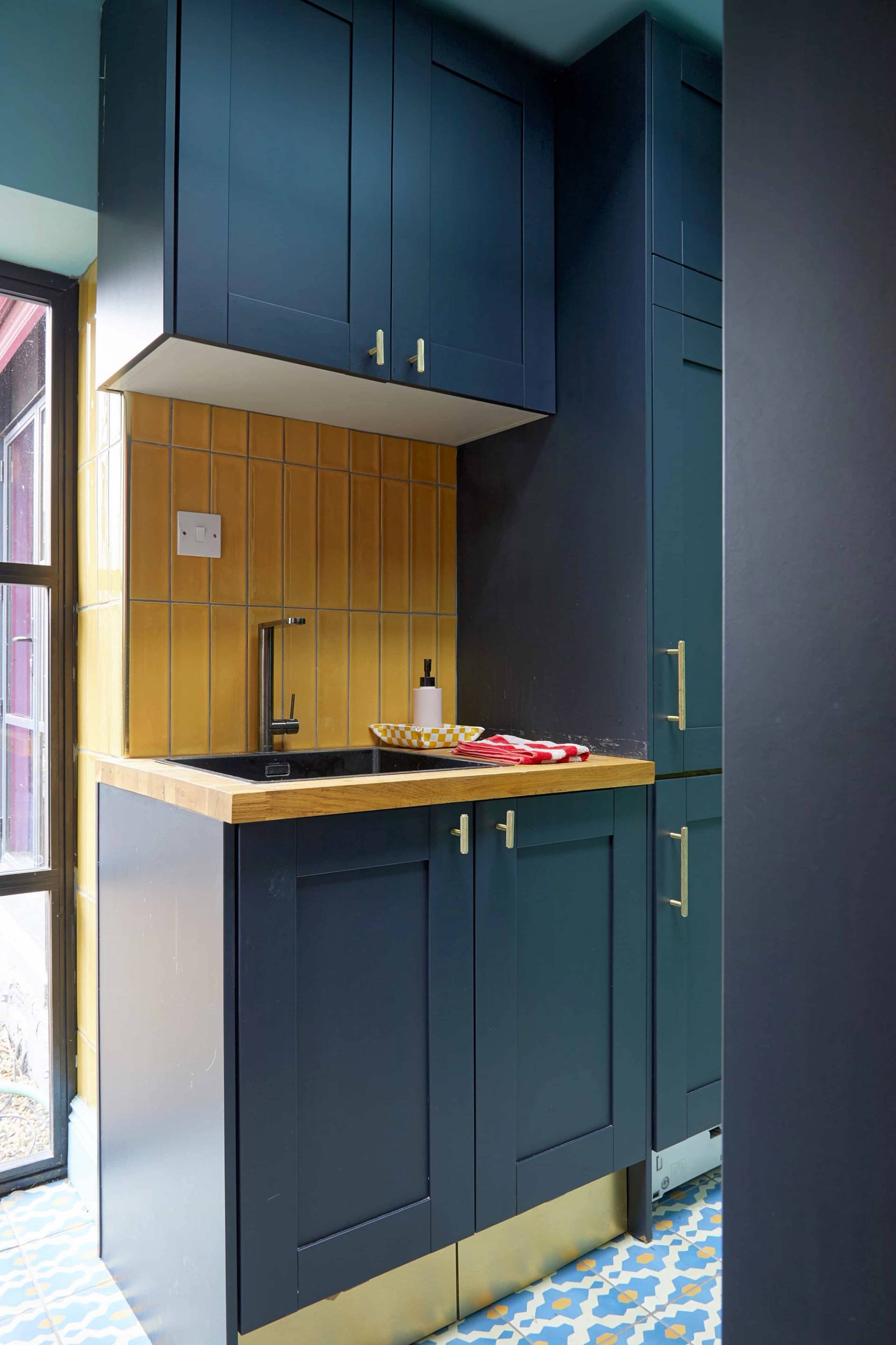 Teal utility kitchen workspace with yellow tile splashback, black counter, and integrated sink, Love Locations SE6.