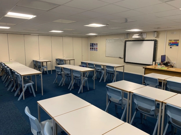 Love Locations bright secondary school classroom Bristol: High school learning room with blue carpeting, modular student desks, and sleek panel partitions, tailored for corporate training videos and drama sets.